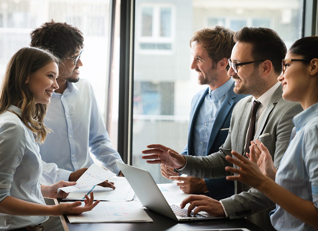 Captive Insurance Management - Small Group of Employees Having a Discussion During a Business Meeting in the Office While Standing Around a Table with an Open Laptop